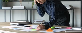 a salesperson on the phone holds a pencil and examines paperwork on a desk