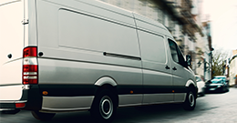 a plain white sprinter van makes a turn on a cobblestone street