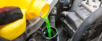 a mechanic pours a green-tinted oil into an engine